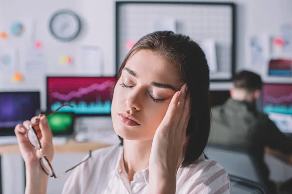 Selective focus of tired data analyst touching head while colleague working in office 